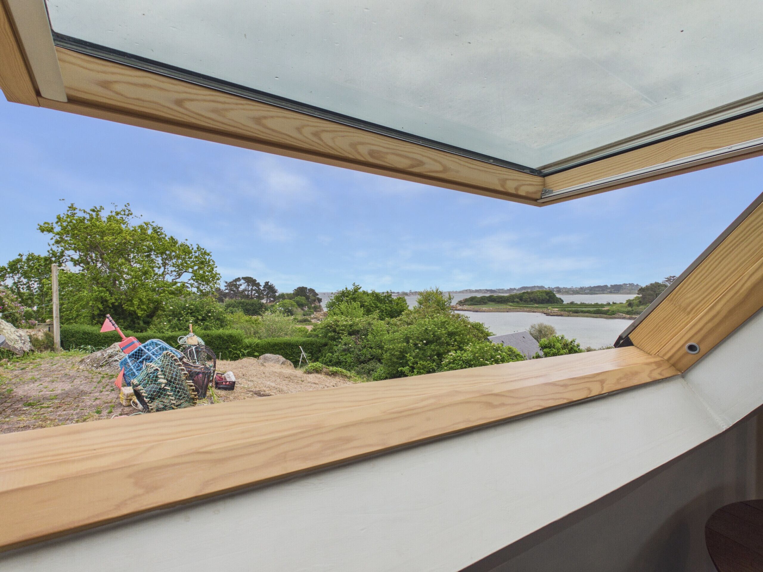 A room with a skylight, a view of a river, and a wooden deck outside.