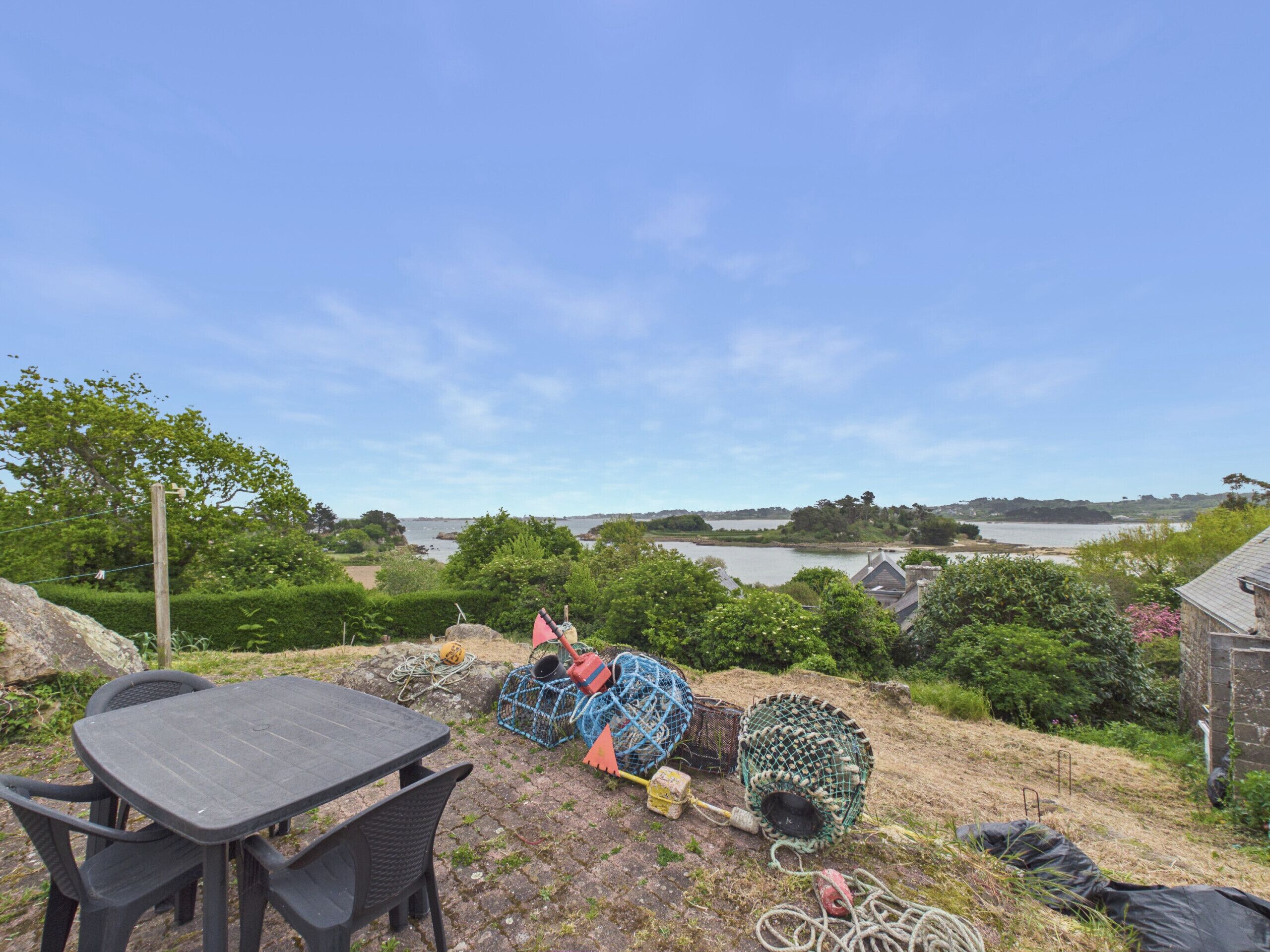 Eine Terrasse mit Tisch und Stühlen, Angelausrüstung und Blick auf einen See und ferne Hügel.