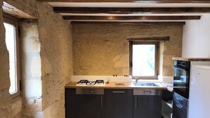A compact kitchen with a stone wall, wooden beams, a window, and modern appliances.