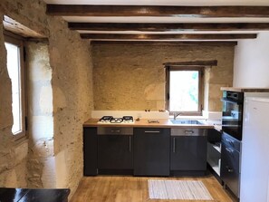 A compact kitchen with a stone wall, wooden beams, a window, and modern appliances. - La p'tite maison ... 3 chb 85mm2 (Sainte-Mondane)
