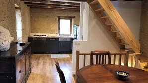A rustic kitchen with exposed beams, a wooden staircase, and a dining area with a wooden table and chairs.