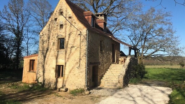 A rustic stone building with a sloped roof, a wooden door, and a staircase leading to the entrance.