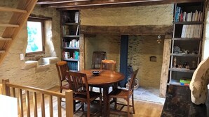 A rustic room with a wooden staircase, a round wooden dining table with chairs, and bookshelves filled with books and decorative items.