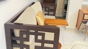 Sala de estar moderna com sofá, mesa lateral de madeira e área de cozinha visível por um arco.