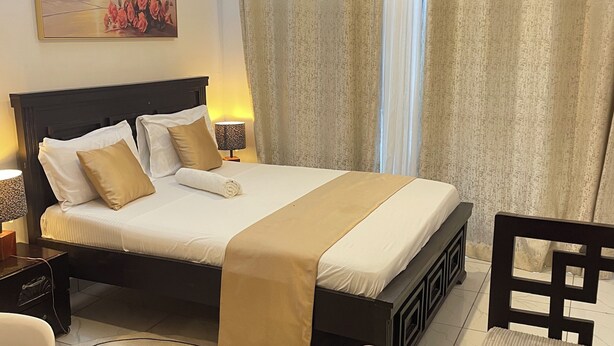 Quarto de hotel com cama, mesas de cabeceira, escrivaninha, cadeira, ventilador de teto e cortinas.