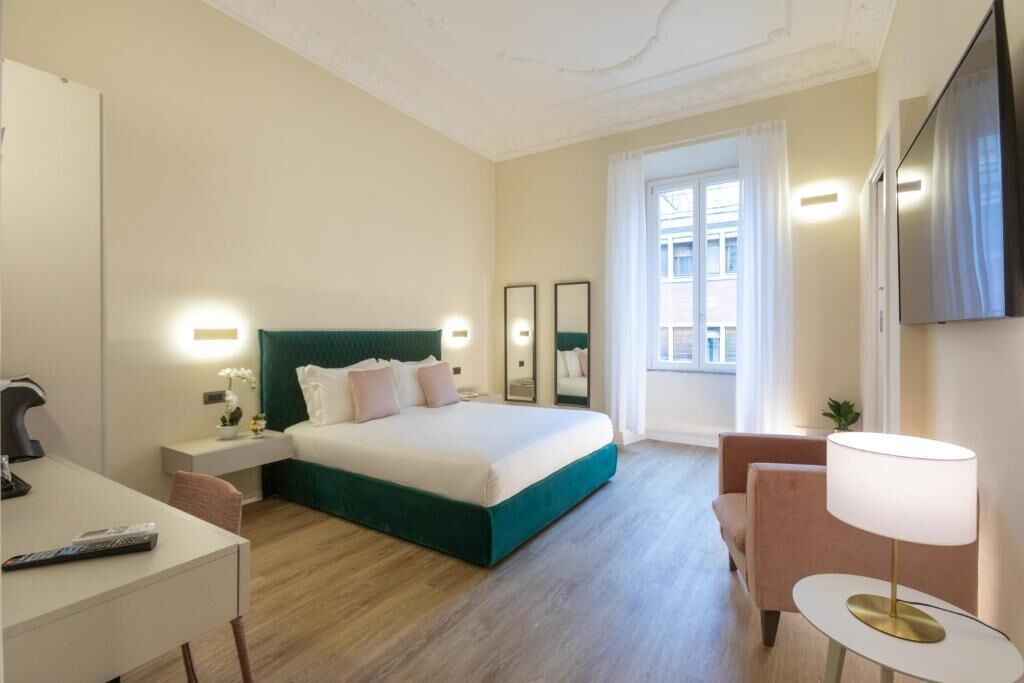A hotel room with a bed, bedside table, lamp, chair, desk, and a TV mounted on the wall.