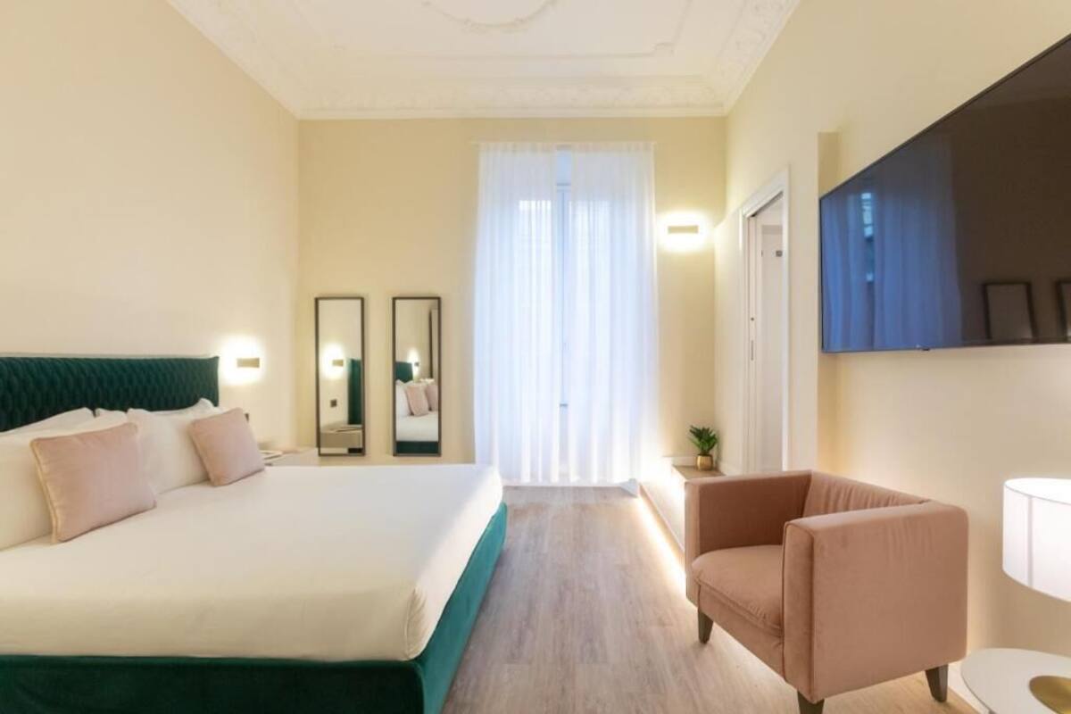 A hotel room with a bed, a chair, a TV, and a window with curtains.