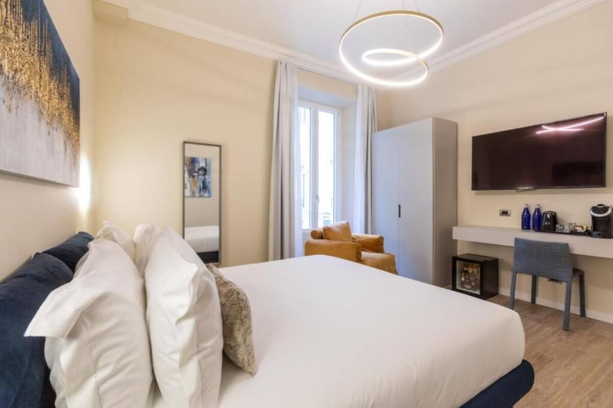 A hotel room with a large bed, a desk, a TV, and a window with curtains.