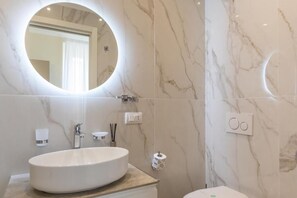 Une salle de bain avec un miroir rond, un lavabo blanc, des toilettes et un mur en marbre.