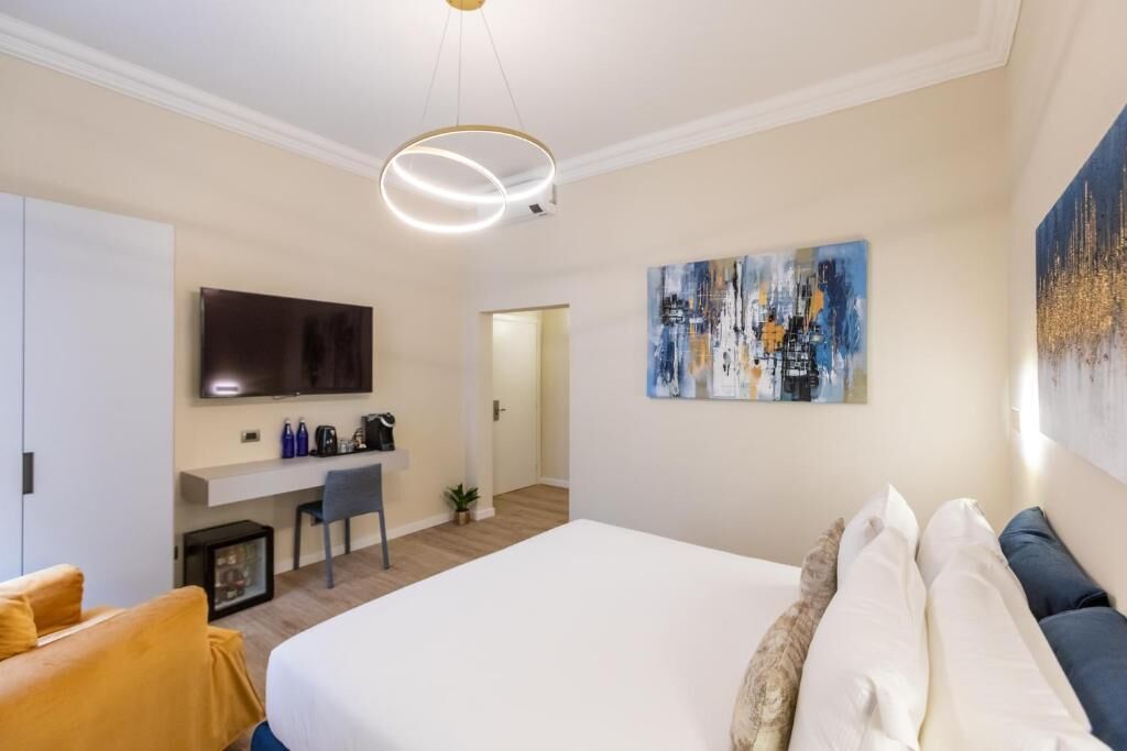A modern hotel room with a large bed, a desk, a TV, and artwork on the walls.
