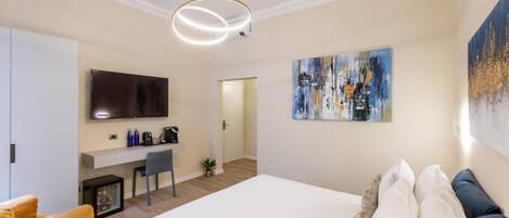 A modern hotel room with a large bed, a desk, a TV, and artwork on the walls.