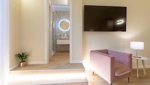 Une chambre d’hôtel moderne équipée d’un téléviseur à écran plat, d’un petit miroir rond, d’un canapé rose, d’une lampe et d’une plante en pot.