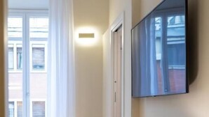 Une chambre moderne avec un canapé, une lampe, un téléviseur et une fenêtre avec des rideaux.