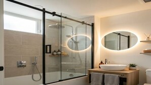 A modern bathroom with a glass-enclosed shower, a round mirror, a wooden vanity, and a white sink. - Hotel with 5 bedrooms and AC in fantastic Lipa City (Lipa City)