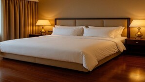 A large bed with white linens, two bedside lamps, and a wooden floor. - Hotel with 5 bedrooms and AC in fantastic Lipa City (Lipa City)
