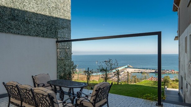 A patio with a table and chairs, a view of the sea, and a building with a textured wall. - Modern Sea View Stay Near Istanbul Airport (İstanbul)