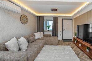 Ein modernes Wohnzimmer mit einem Ecksofa, einem Flachbildfernseher und einem fußbodenbelag mit Fischgrätmuster.