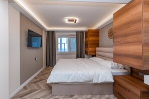 Ein Schlafzimmer mit einem Bett, einem an der Wand befestigten Fernseher, einem Fenster mit Vorhängen und einem Holzschrank.