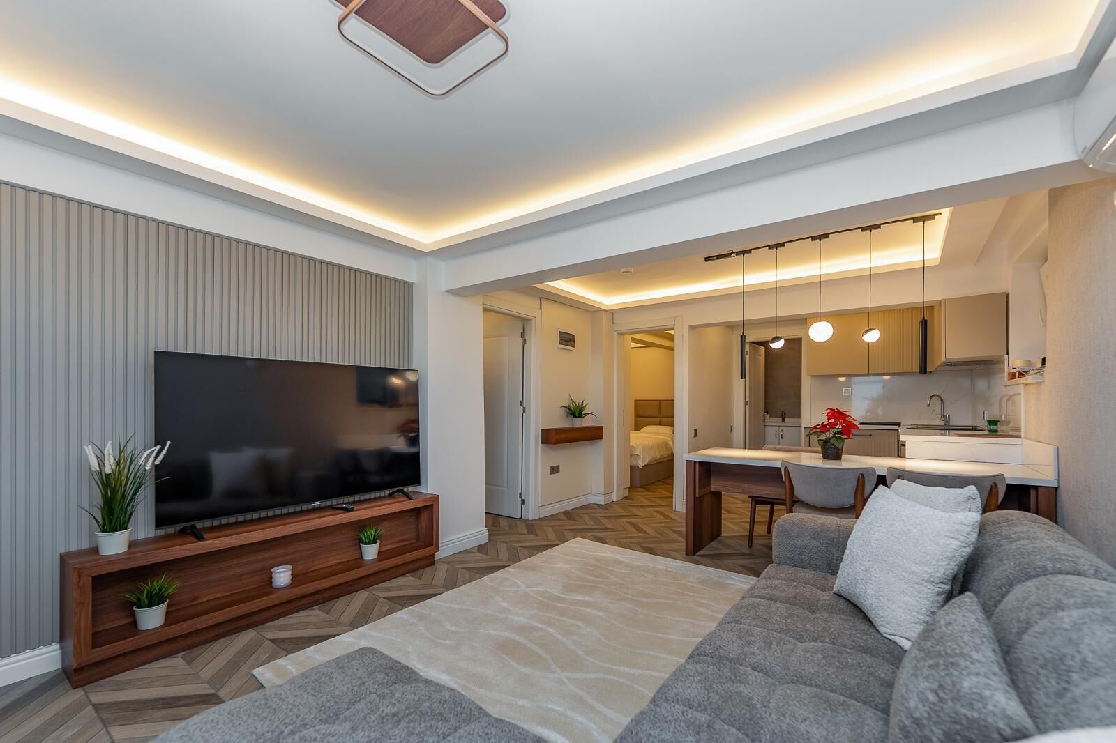 Een moderne woonkamer met een flatscreen televisie, een grijze bank, een houten entertainmentkast en een visgraatvloer.