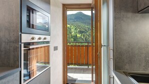 A kitchen with a view of a forested mountain. - Apartment "Cima Piazzi" – Comfort, Relaxation, and Nature between Bormio and Livigno (Semogo)