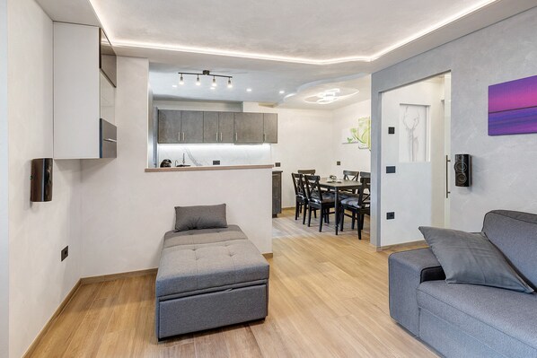 Una sala moderna con un sofá gris, un reposapiés y un comedor con mesa y sillas.