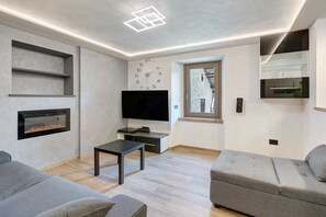 Uma sala de estar moderna com televisão de tela plana, lareira, sofá e uma mesa pequena.