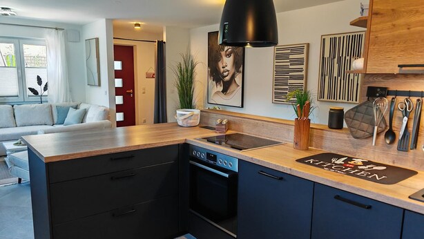A modern kitchen with a central island, black cabinetry, and a wooden countertop. - Apartment 'City High Mountain' with Private Terrace, Private Garden and Wi-Fi (Brunnthal)