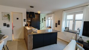 A modern kitchen with a central island, a dining area with a white sofa, and a TV on a stand. - Apartment 'City High Mountain' with Private Terrace, Private Garden and Wi-Fi (Brunnthal)