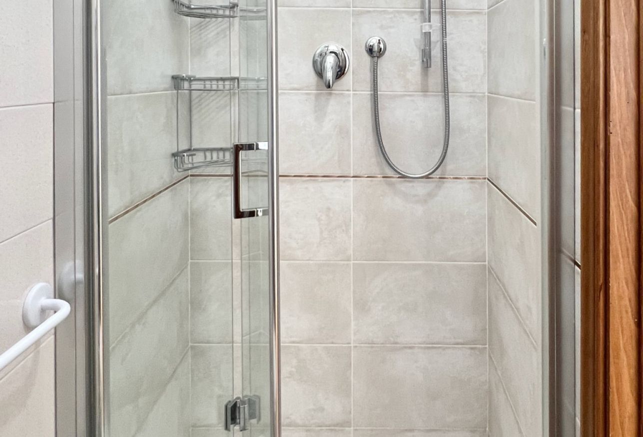 A shower with a glass door, a chrome showerhead, and a handheld shower attachment.