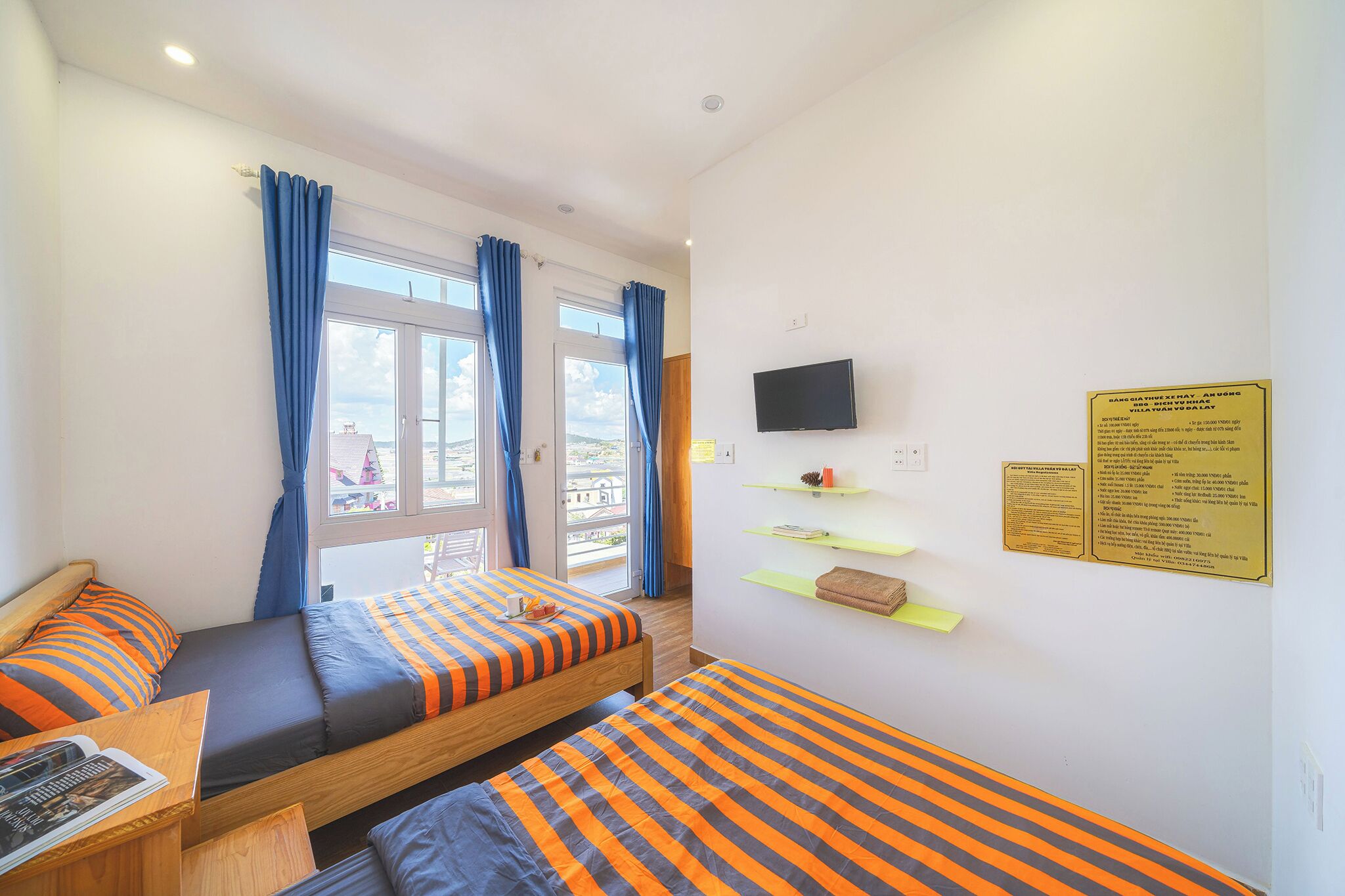Une chambre d’hôtel avec deux lits, une télévision, une fenêtre avec des rideaux et une étagère fixée au mur sur laquelle est posée une serviette.