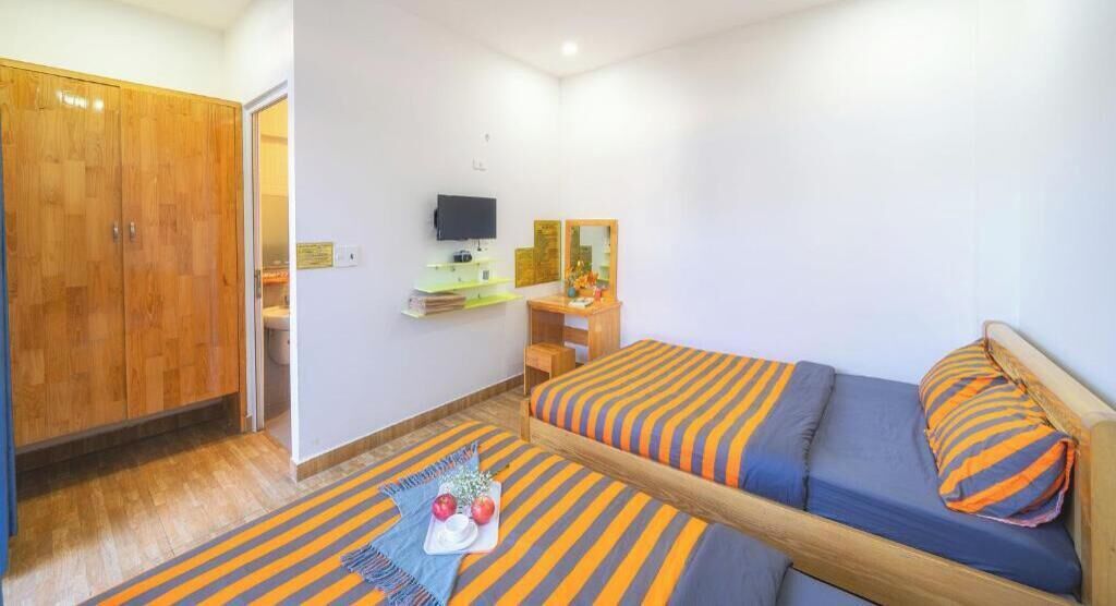 A bedroom with a bed, a wooden wardrobe, a desk with a mirror, and a television.