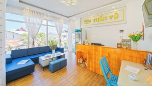 Vestíbulo de hotel con mostrador de recepción, un sofá azul, una pequeña mesa y vistas al exterior.