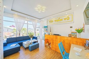 Um saguão de hotel com balcão de recepção, um sofá azul, uma mesinha e vista para o exterior.