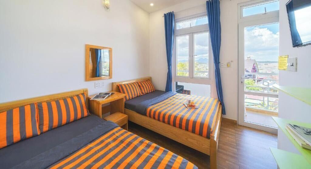A room with two beds, a wooden nightstand, a mirror, a window with curtains, and a view of the outside.
