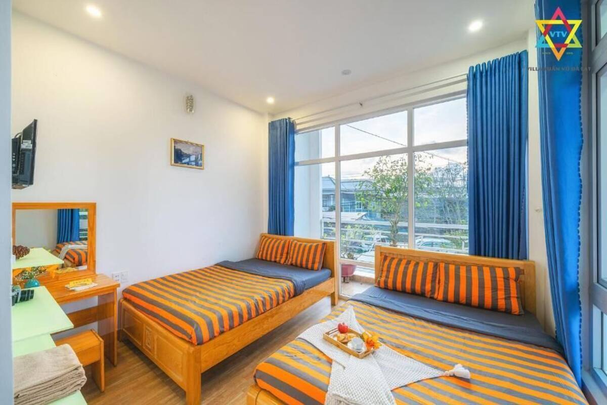 Habitación de hotel con dos camas, un escritorio, una silla, un ventanal con cortinas y vistas al exterior.