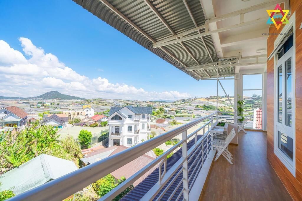 A balcony with a view of a residential area, a metal roof, and a wooden floor.