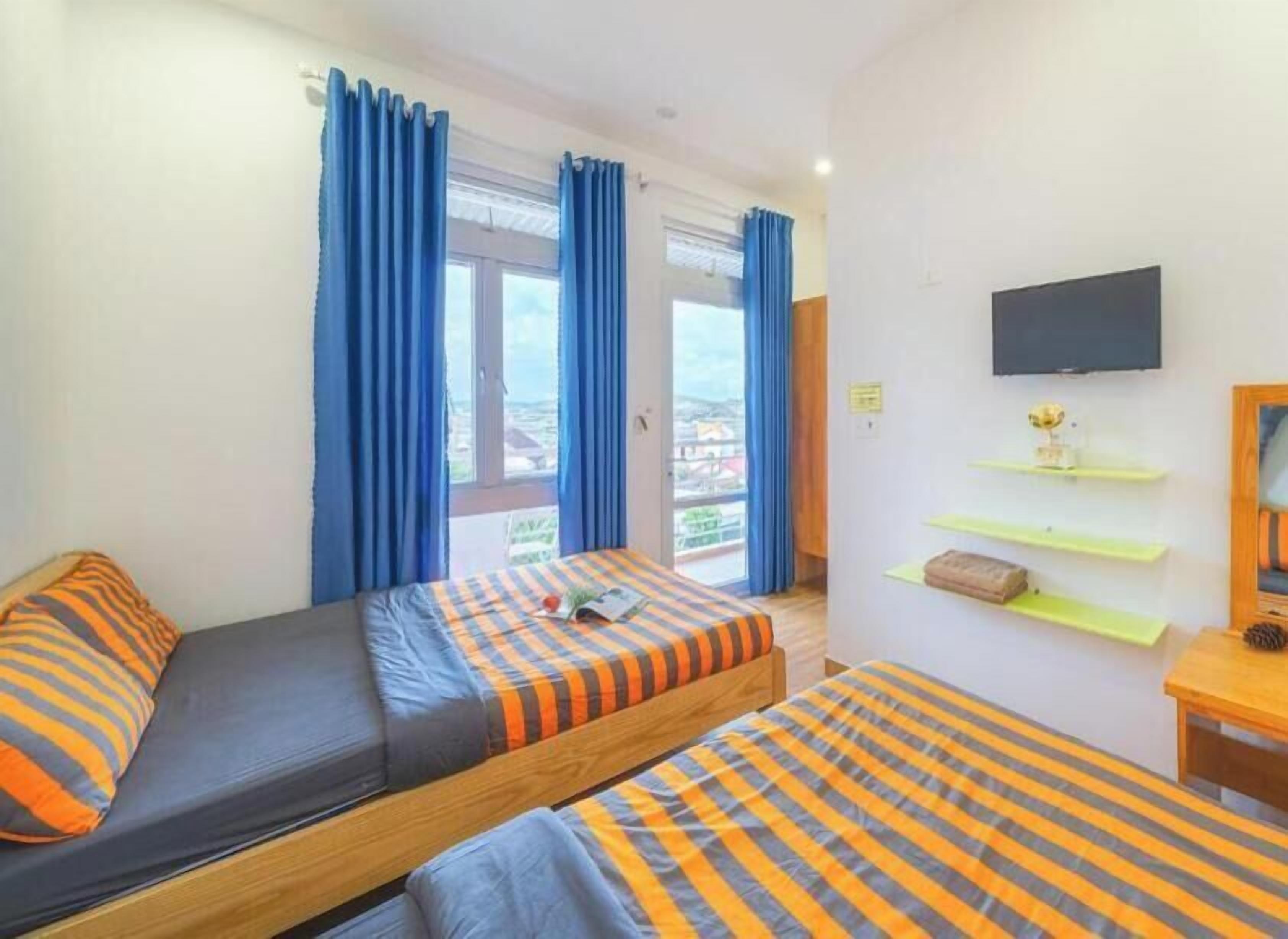Une chambre avec deux lits, une télévision et un balcon agrémenté de rideaux bleus.