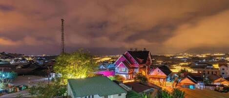A nighttime view of a coastal town with brightly lit houses and a prominent communication tower.