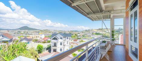 A balcony with a view of a residential area, a metal roof, and a wooden floor.
