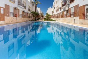 A swimming pool with a clear blue water surface, surrounded by multi-story buildings with balconies and brick facades. - Cabanas Escape - Pool & Terrace Near the Beach (Cabanas)