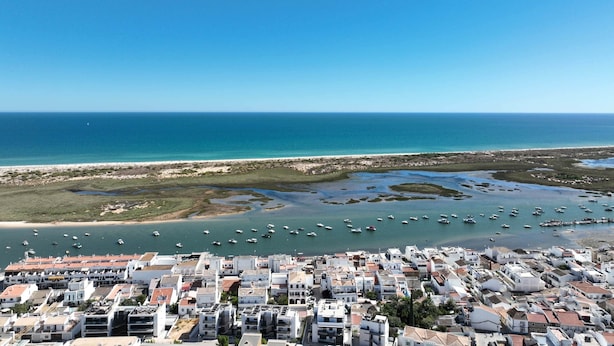 Un pueblo costero con un puerto deportivo, edificios blancos y un cielo azul despejado.