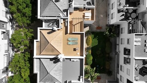Vista aérea de un edificio residencial con varios balcones, una terraza en la azotea y vegetación circundante.