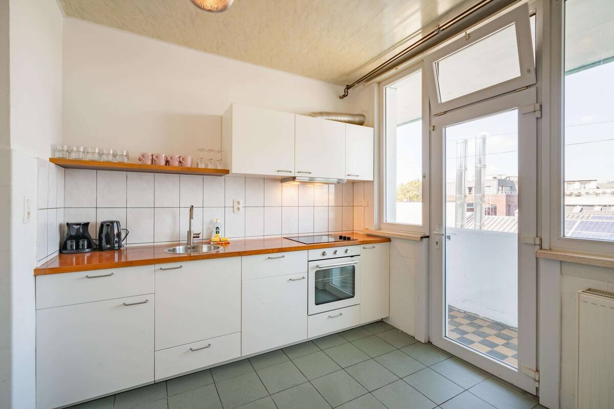 Een keuken met witte kasten, een houten aanrecht, een fornuis en een raam met uitzicht op gebouwen.