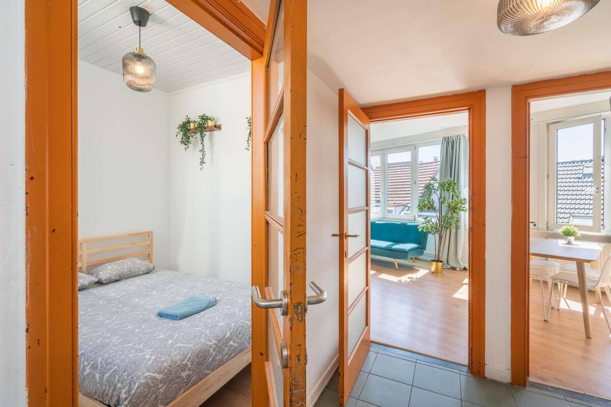 Een slaapkamer met een bed, een deur naar een zithoek met een bank en een tafel.
