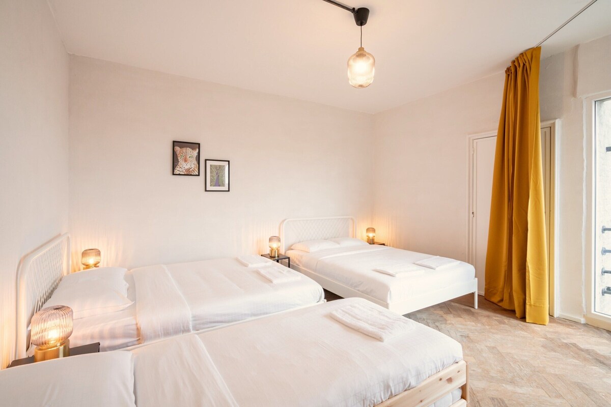 Una habitación de hotel con dos camas, una lámpara en el techo y una ventana con cortinas.