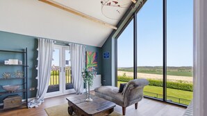 Ein geräumiges Zimmer mit einer großen Schiebeglasdoor zum Balkon, ein grauer Sessel, ein Holztisch und Blick ins Grüne.