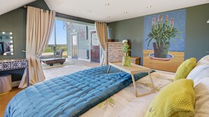 Ein Schlafzimmer mit einem großen Bett, einem Schminktisch mit Beleuchtung, einem Schrank, einem Gemälde und Blick ins Freie.