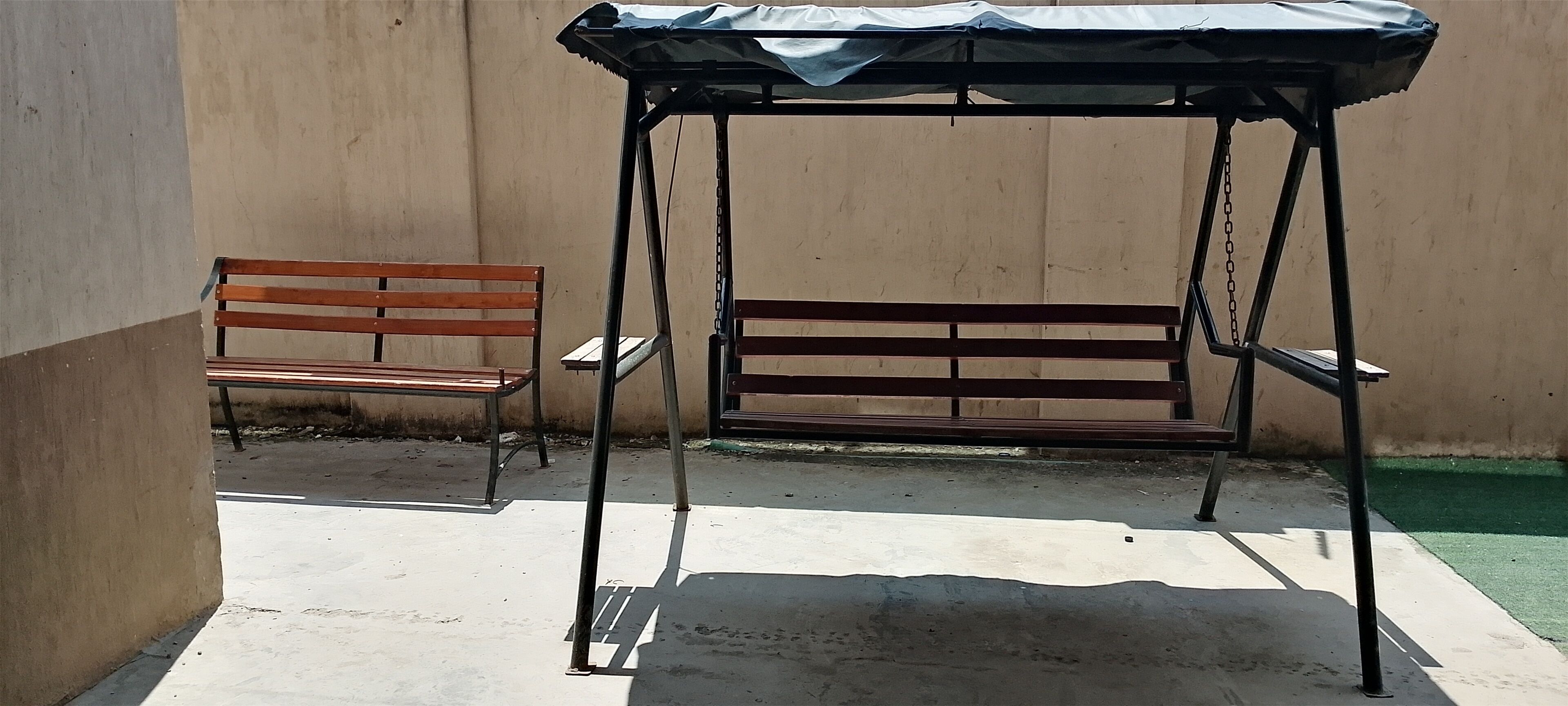 Une structure de jeu en métal avec des balançoires, un banc, une chaise et un sol en béton.