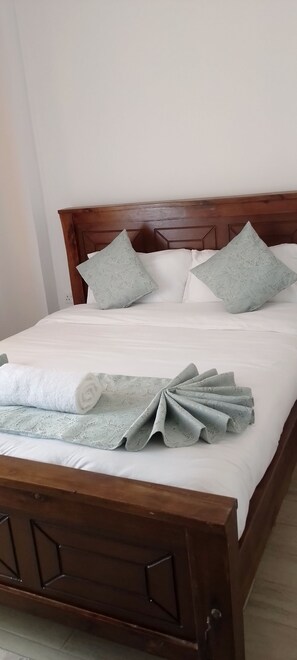 A neatly made bed with a wooden headboard, white bedding, and decorative pillows. - Perfect 1-bedroom apartment with AC in peaceful Nairobi (Nairobi)