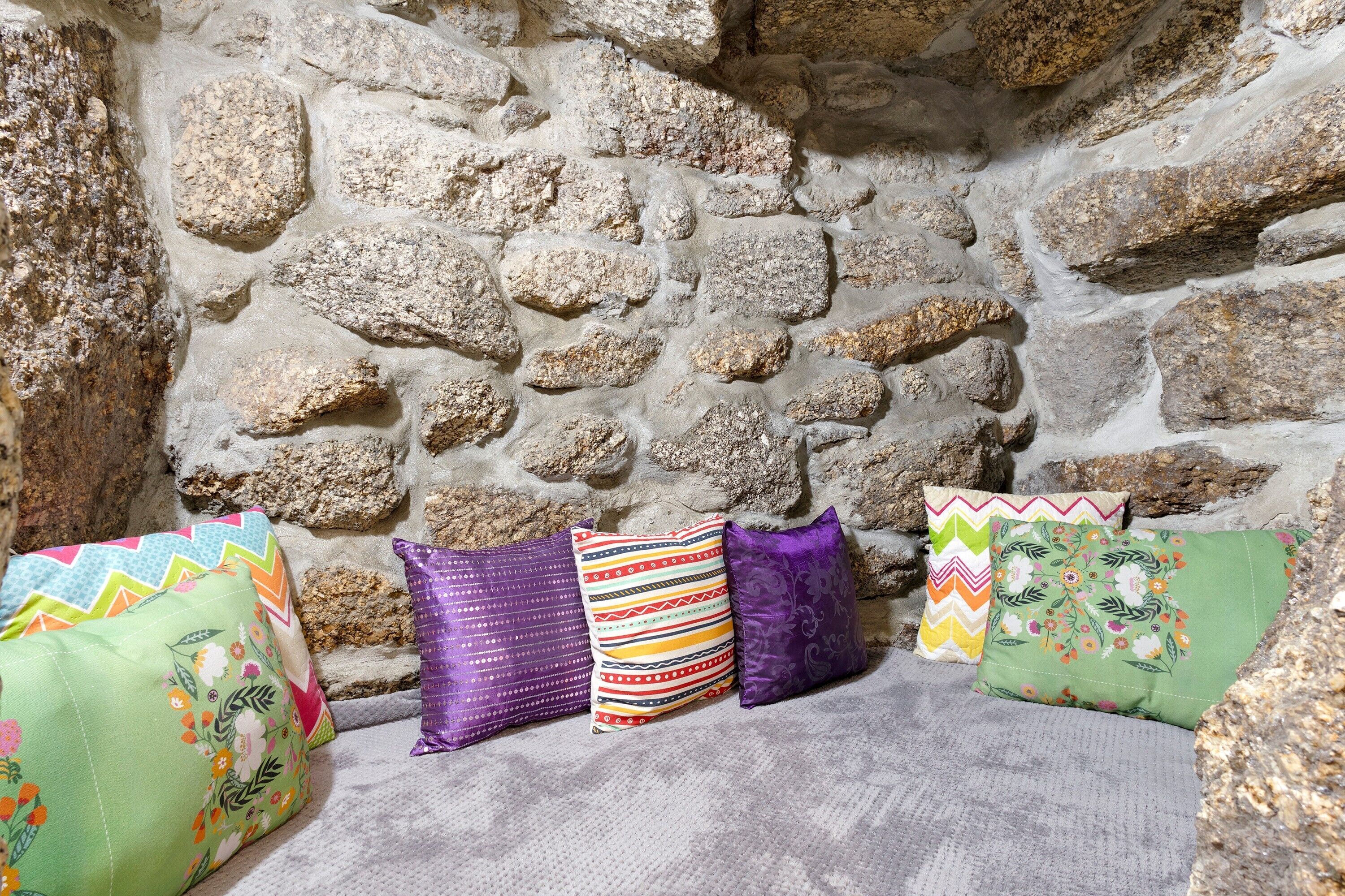 Un muro de piedra con un banco y almohadones coloridos.